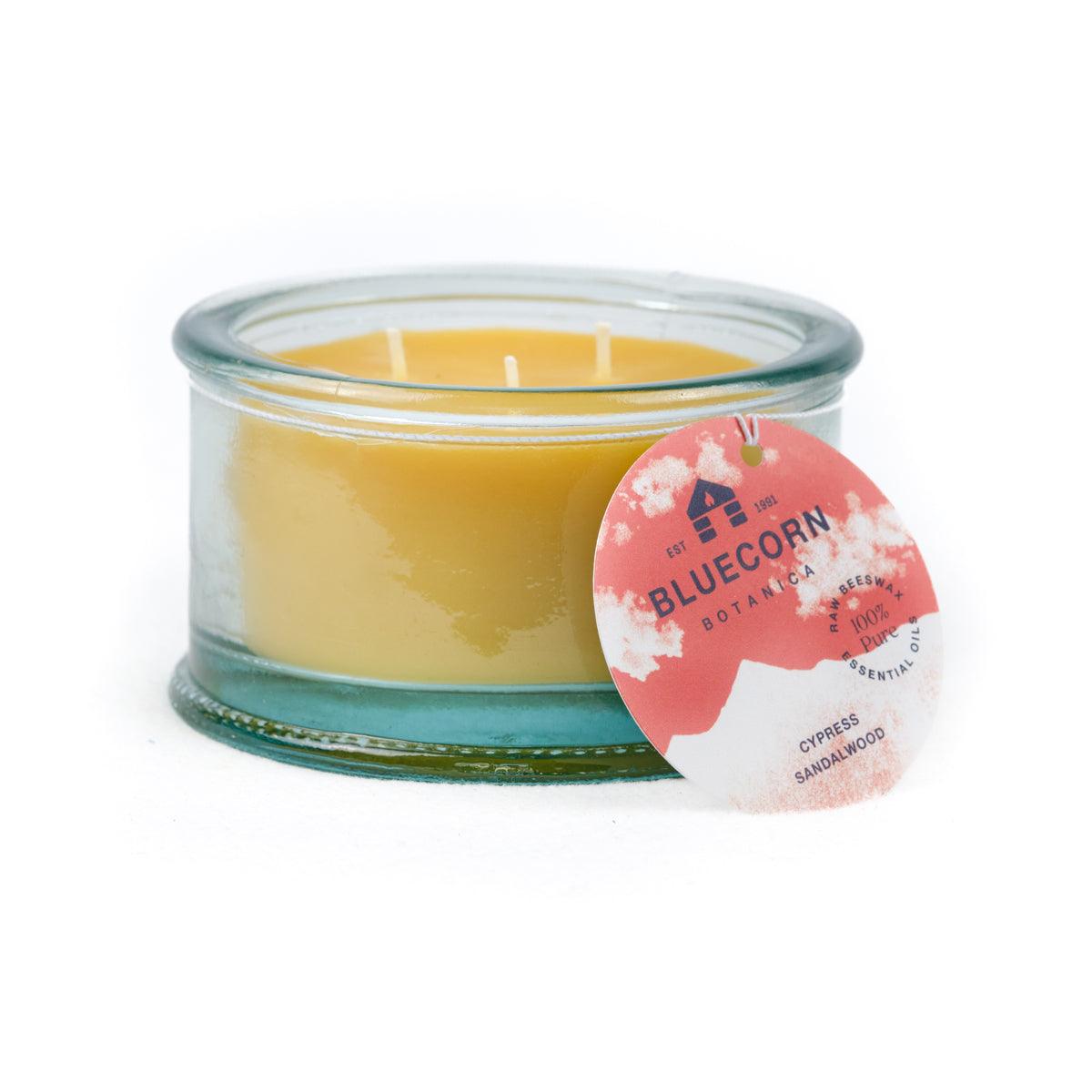 Bluecorn Botanica 100% Pure Beeswax Cypress and Sandalwood 10oz 3-Wick Glass Candle. Wax is golden in color and glass is clear colored, with a white back drop. Features red Bluecorn Botanica hang tag printed on 100% recyled paper with Bluecorn name and logo. Burn Time: 18 hours.  Made with 100% Pure Beeswax, 100% Pure Essentail Oils and a 100% pure cotton wick, no lead. Candles are paraffin free, clean burning and non-toxic. 