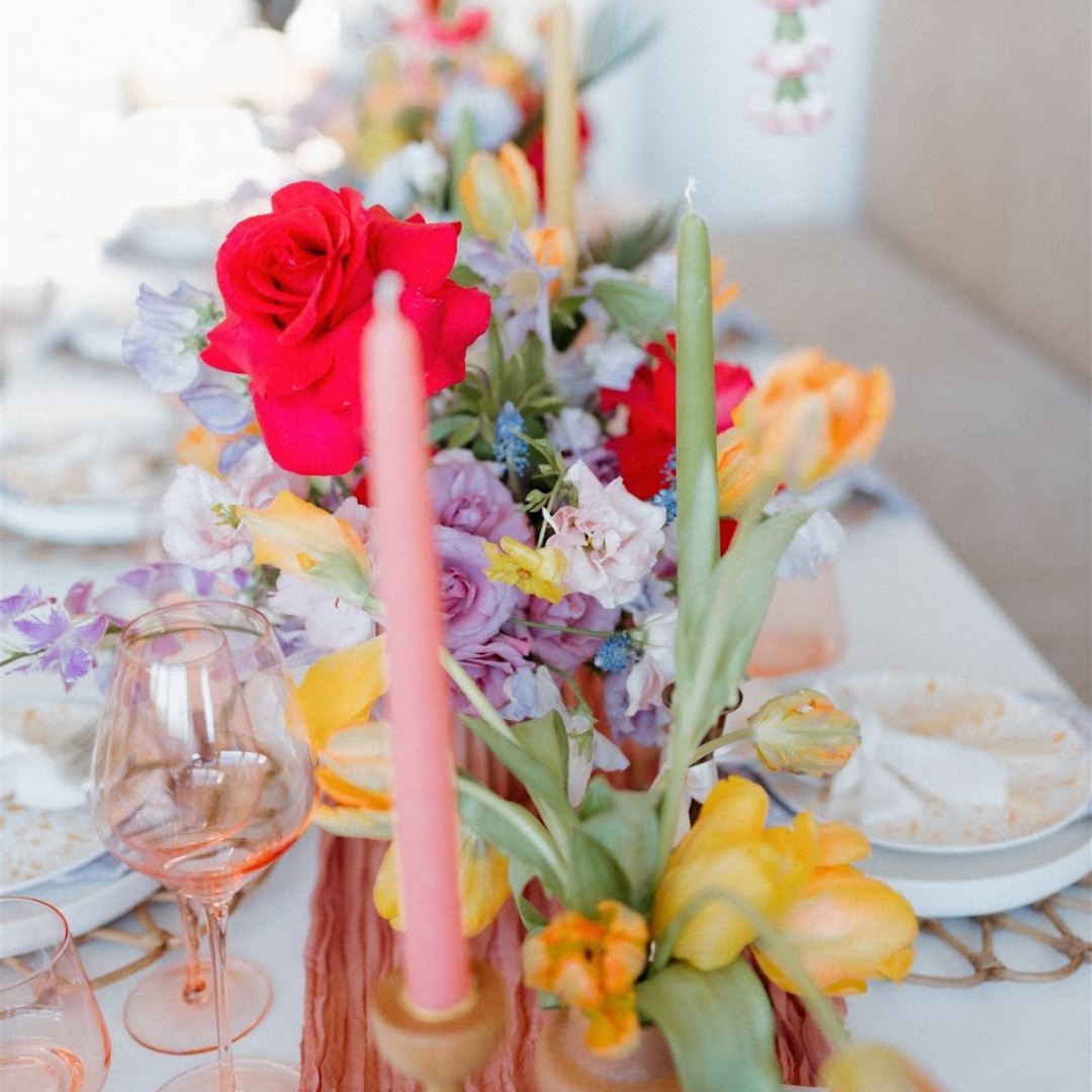 light pink taper candle from bluecorn candles in front of a floral spring table with green candlesticks